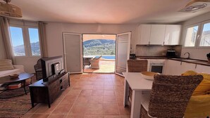 A modern kitchen with white cabinets, a dining table, and a view of a mountainous landscape through an open door.