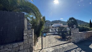 A gated entrance with a stone wall, a palm tree, and a mountain in the background.