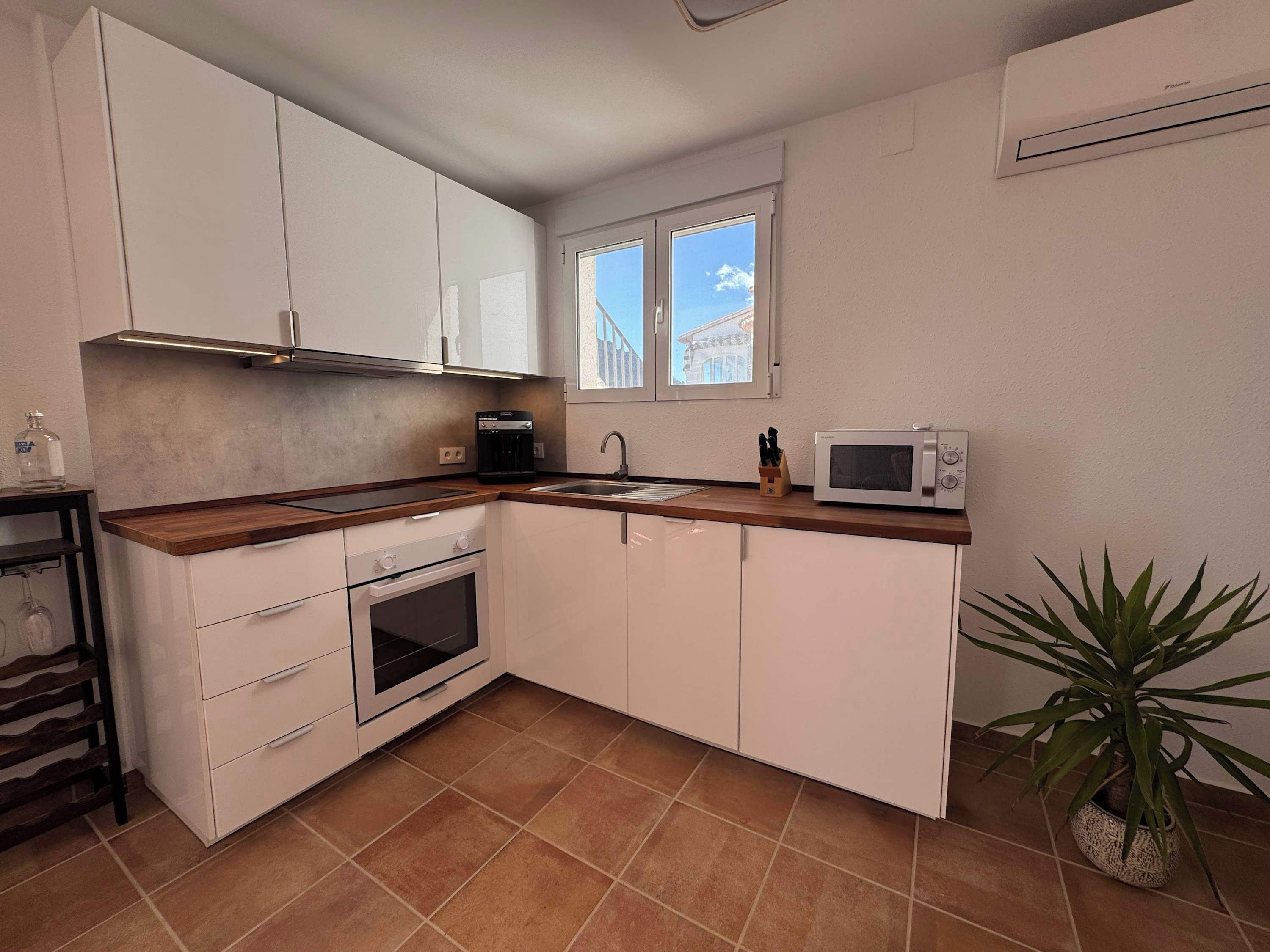 A compact kitchen with white cabinets, a built-in oven, a microwave, and a window with a view of a building.