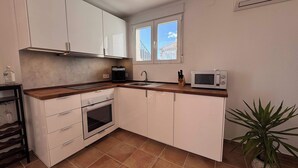 A compact kitchen with white cabinets, a built-in oven, a microwave, and a window with a view of a building.