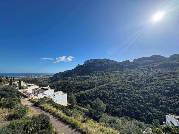 A mountainous landscape with a clear sky, a path leading to a building, and distant views of the sea.