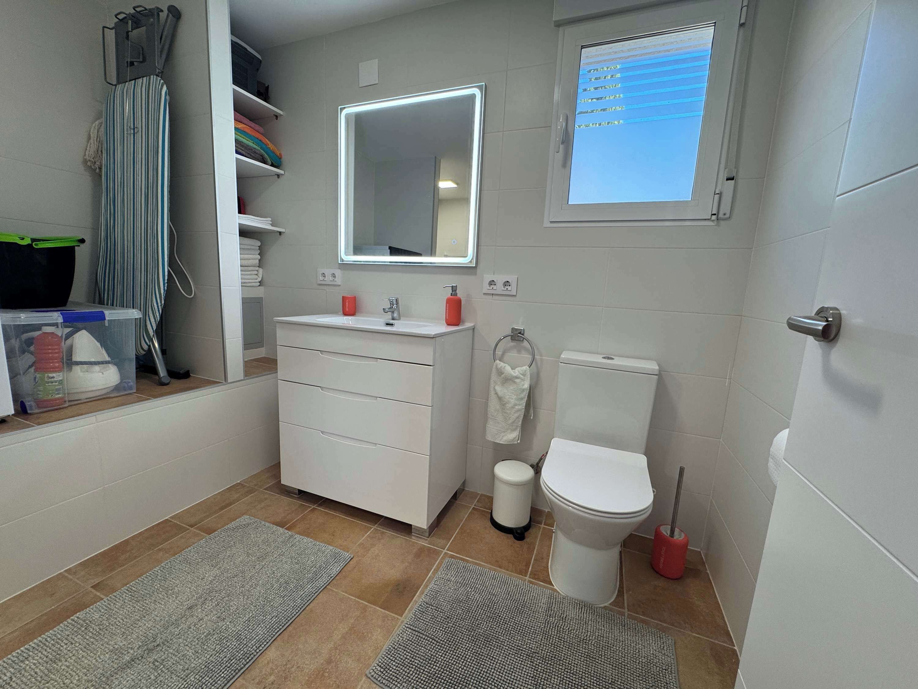 Een badkamer met een wit wastafel, spiegel, toilet en een raam met uitzicht op de lucht.