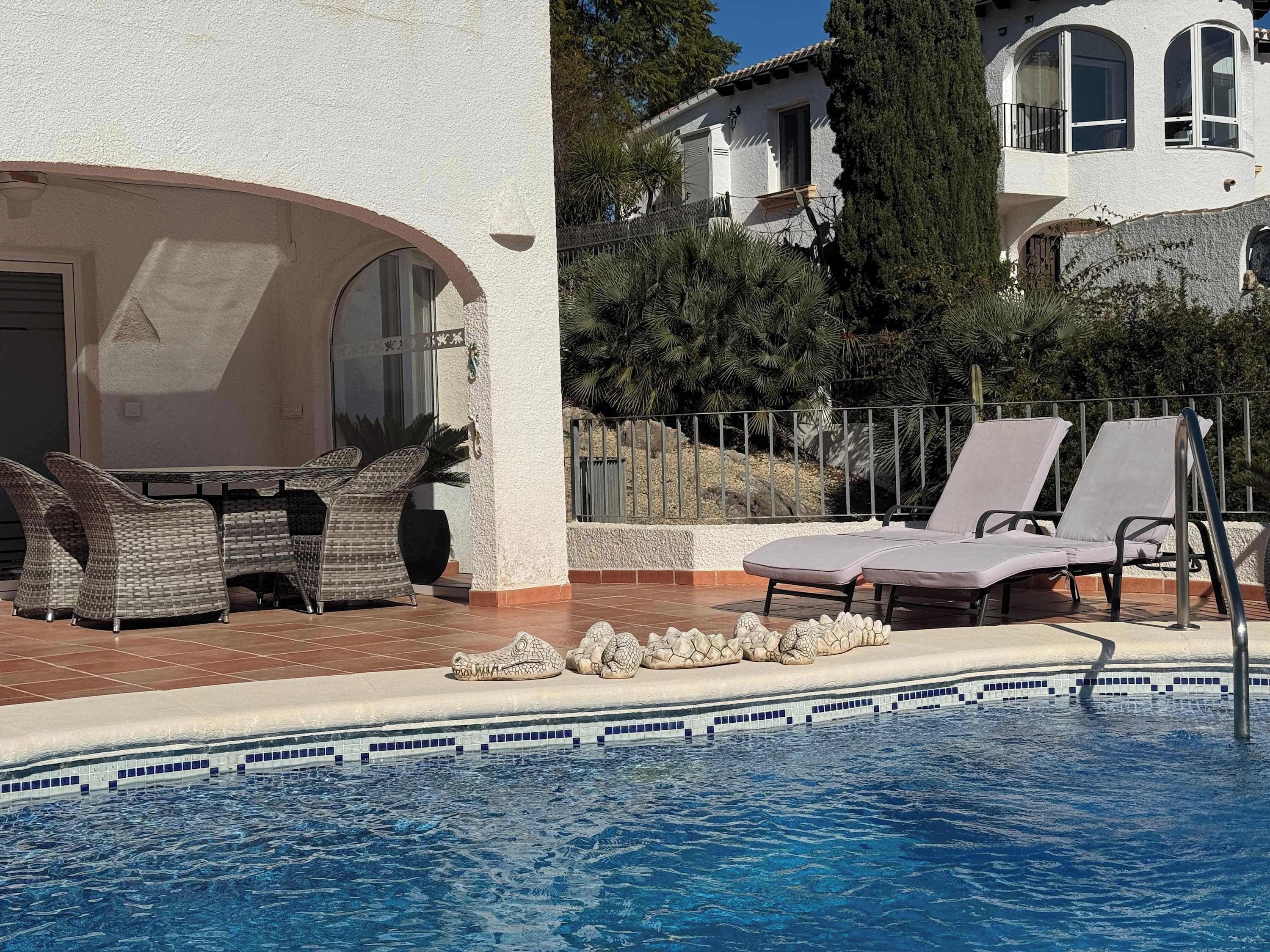 A pool area with lounge chairs, a dining table, and a decorative stone arrangement.