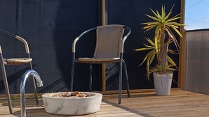 A wooden deck with a hot tub, two wicker chairs, and a potted plant.