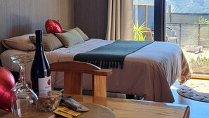 A bedroom with a bed, a wooden table with a bottle and snacks, and a view of the outdoors.