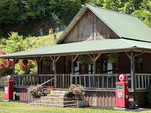 Un bâtiment rustique en bois, doté d’un porche, d’un escalier en pierre et d’une enseigne de station-service.