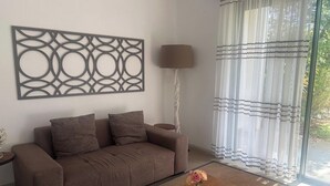 A living room with a brown sofa, a lamp, a coffee table with a vase, and a decorative wall piece. - Luxury apartment in Azuri, Mauritius (Rivière du Rempart)