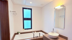 A modern bathroom with a large bathtub, a sink with a bowl, a mirror, and a window. - Luxury apartment in Azuri, Mauritius (Rivière du Rempart)