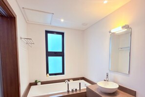Ein modernes Badezimmer mit einer großen Badewanne, einem Waschbecken, einem Spiegel und einem Fenster.