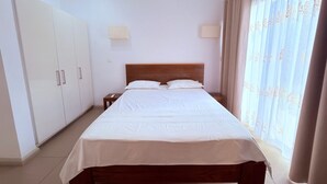 A bedroom with a bed, wardrobe, bedside lamps, and curtains. - Luxury apartment in Azuri, Mauritius (Rivière du Rempart)
