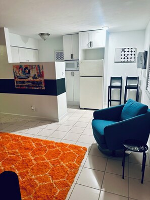 A modern kitchen with white cabinets, a microwave, and a refrigerator. There is a blue sofa and an orange rug in the living area. - Serene 1-bedroom & 1-bathroom in Wilton Manor (Fort Lauderdale)