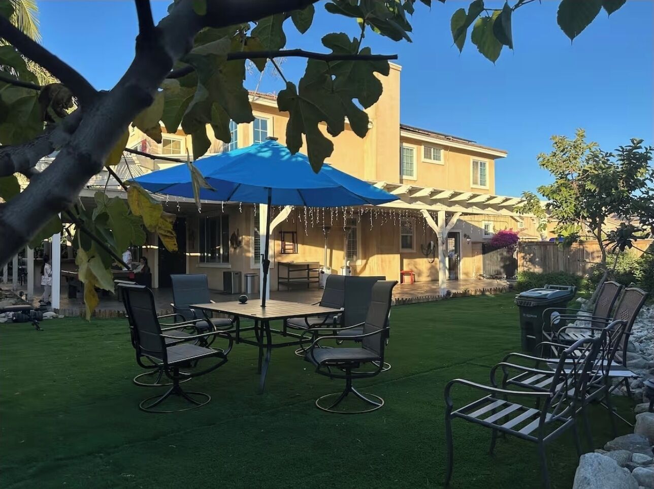 Eine Terrasse mit Tisch und Stühlen, einem blauen Sonnenschirm und einem Gebäude im Hintergrund.