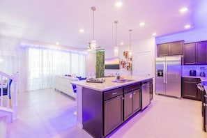 Une cuisine moderne dotée d’un îlot central, d’appareils électroménagers en acier inoxydable et de luminaires suspendus.
