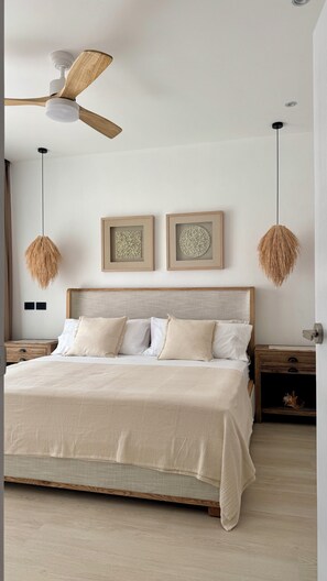 Un dormitorio con una cama, cabecera de madera, dos cuadros colgados en la pared, un ventilador de techo e iluminación colgante.