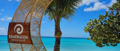 Un panneau indiquant l’entrée d’un club de plage, avec un palmier et un hamac.