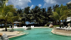 A clear pool with lounge chairs, palm trees, and a gazebo. - Aqua Esmeralda • Luxury Beachfront • Curazao 103 (Dominicus)