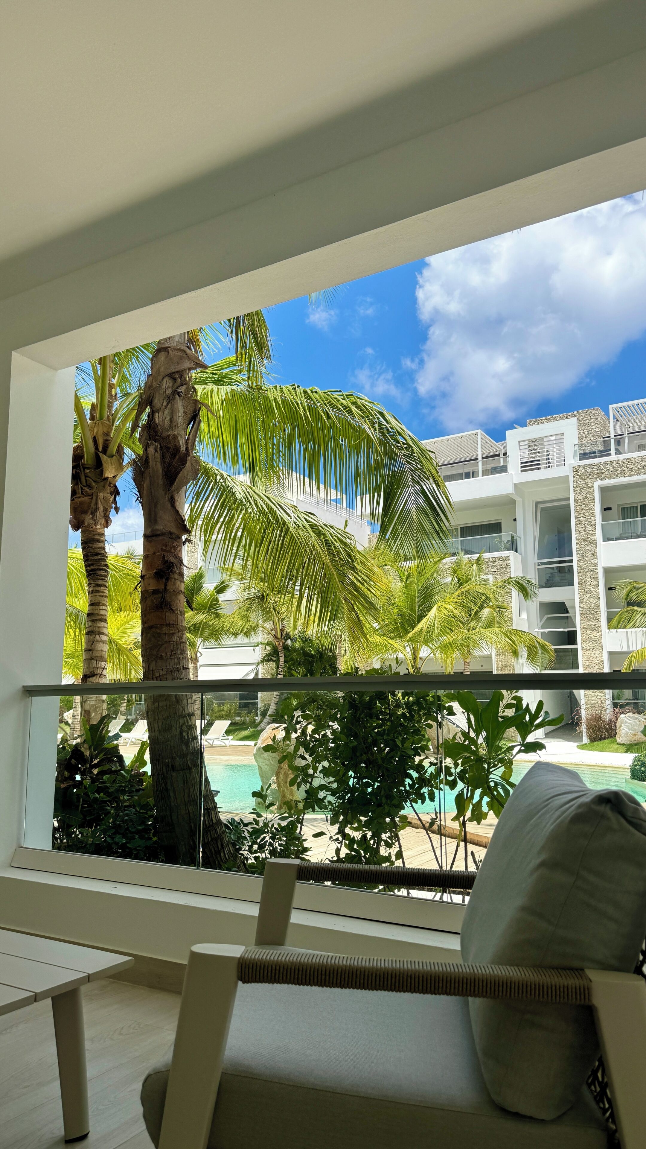 Een balkon met uitzicht op een zwembad, palmbomen en een modern gebouw.