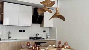 A modern kitchen with white cabinets, a round dining table with wicker chairs, and hanging wicker pendant lights. - Aqua Esmeralda • Luxury Beachfront • Curazao 103 (Dominicus)