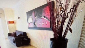 Un salón con sofá, una mesa de centro, una planta en maceta y un cuadro en la pared.