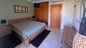 Un dormitorio con una cama, una mesita de noche, un cuadro enmarcado, una puerta y un equipo de aire acondicionado.