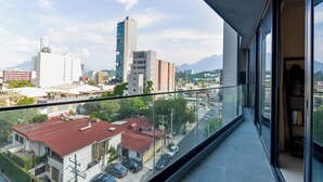 A cityscape view from a balcony with modern buildings, a clear sky, and a distant mountain range. - Niza (Monterrey)