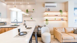 A modern kitchen with a central island, bar stools, a sofa, and a hanging plant. - Niza (Monterrey)