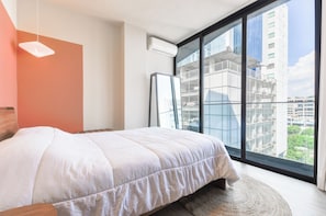 A modern bedroom with a large window, a bed, and a wall-mounted air conditioner. - Niza (Monterrey)