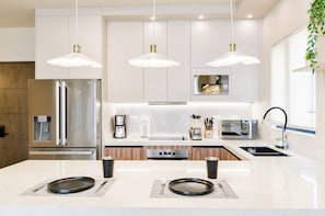 A modern kitchen with stainless steel appliances, pendant lighting, and a central island with seating. - Niza (Monterrey)