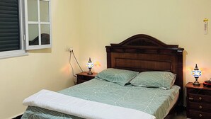 A bedroom with a bed, two bedside tables, a window, and a ceiling light fixture. - Amazigh host Taroudannt (Taroudant)