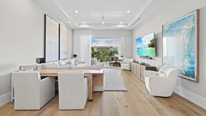 A modern living room with a sofa, chairs, a TV, and artwork on the walls. - Olde Naples Gem | Beach, Dining & Resort Style Living (Naples)
