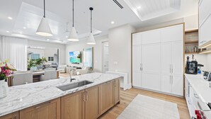 A modern kitchen with a marble countertop, wooden cabinets, pendant lighting, and a large white refrigerator. - Olde Naples Gem | Beach, Dining & Resort Style Living (Naples)