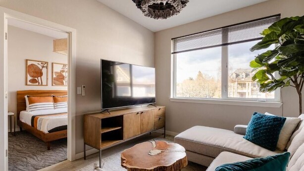 Una sala de estar moderna con cama, televisor y un ventanal grande.