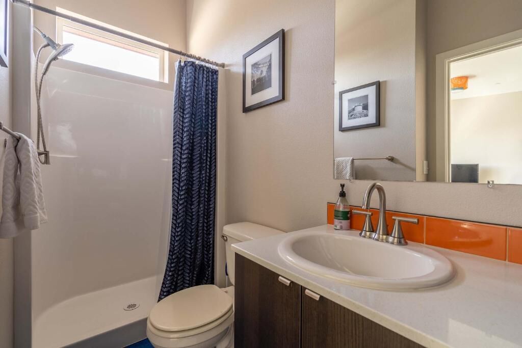A bathroom with a shower, toilet, sink, and two framed pictures on the wall.