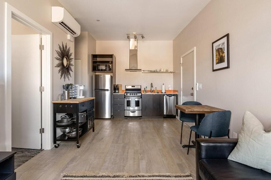 A modern kitchen with stainless steel appliances, a wooden dining table, and a black leather sofa.