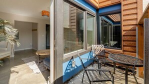 Una habitación moderna con ventanas amplias, una puerta corredera y un pequeño espacio de descanso con una mesa y sillas.