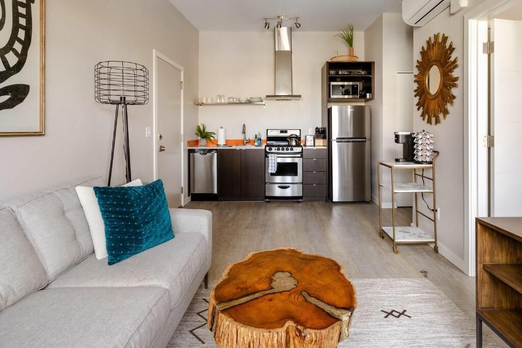 Une cuisine moderne équipée d’appareils électroménagers en acier inoxydable, un coin repas avec une table en bois et un salon agrémenté d’un canapé et d’un tapis décoratif.