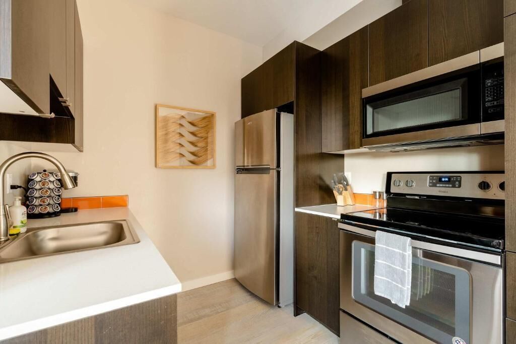 A modern kitchen with stainless steel appliances, a white countertop, and wooden cabinets.