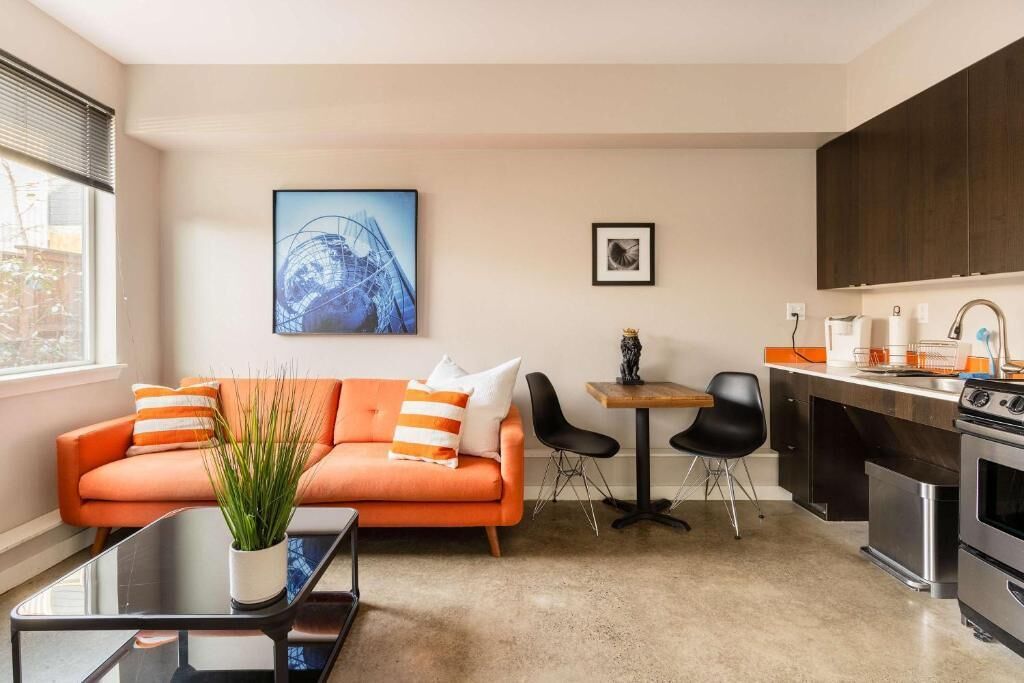 A modern living room with a sofa, coffee table, and chairs, a small dining table, and a kitchen area with appliances.