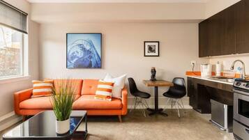 A modern living room with a sofa, coffee table, and chairs, a small dining table, and a kitchen area with appliances.