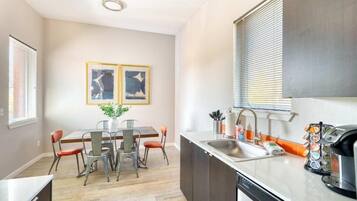 Una cocina moderna con lavavajillas, pileta y cafetera. Hay una mesa de comedor con sillas y dos cuadros en la pared.