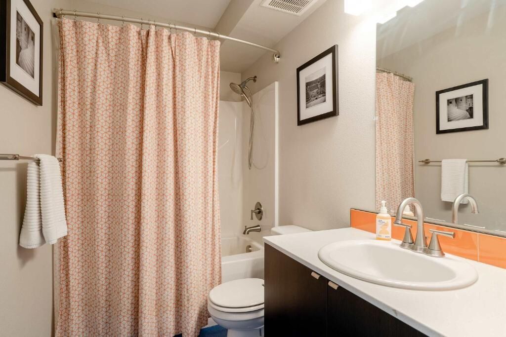 A bathroom with a shower curtain, toilet, sink, and two framed pictures on the wall.