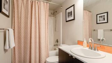 A bathroom with a shower curtain, toilet, sink, and two framed pictures on the wall.
