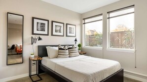 Un dormitorio moderno con una cama grande, una mesita de noche, un espejo y cuadros en la pared.