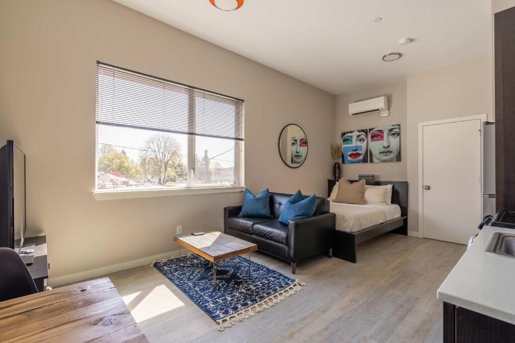 A compact living space with a sofa, a bed, a coffee table, and a window with blinds.
