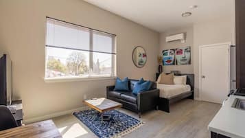 A compact living space with a sofa, a bed, a coffee table, and a window with blinds.