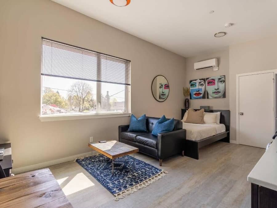 A compact living space with a sofa, a bed, a coffee table, and a window with blinds.