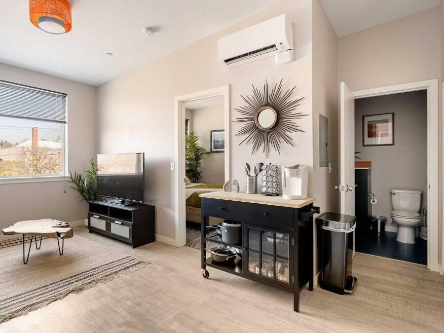 A modern kitchen with a black countertop, a sink, and a stove. There is a window with blinds, a ceiling fan, and an air conditioning unit.