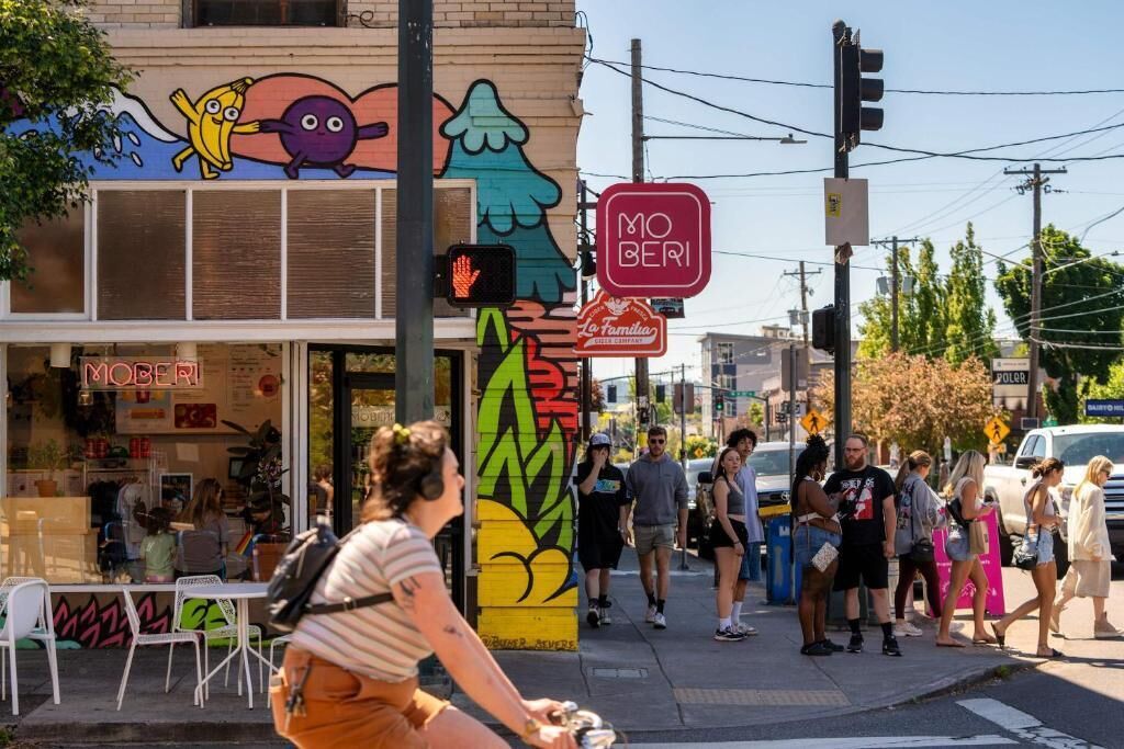 A street scene with a building featuring a colorful mural, a Mo' Berri sign, and a pedestrian crossing.