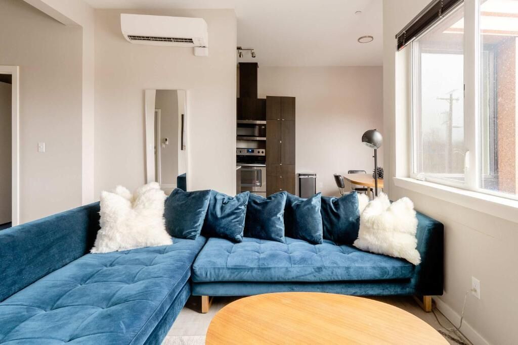 A modern living room with a sectional sofa, a round wooden coffee table, and a view of the kitchen area.
