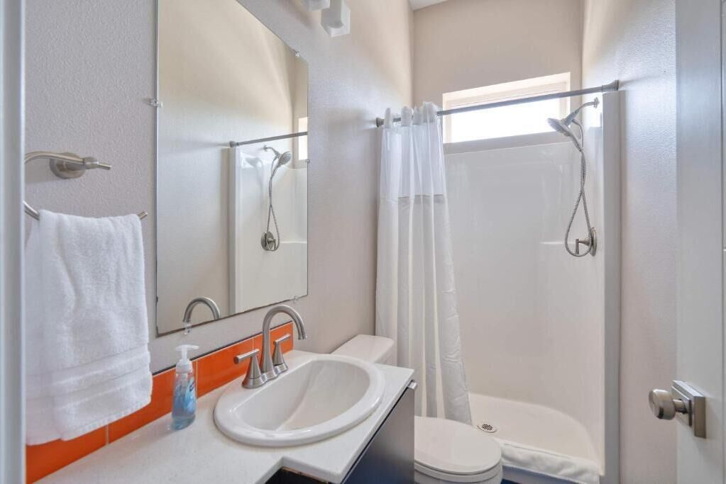 A bathroom with a sink, mirror, shower, and toilet.